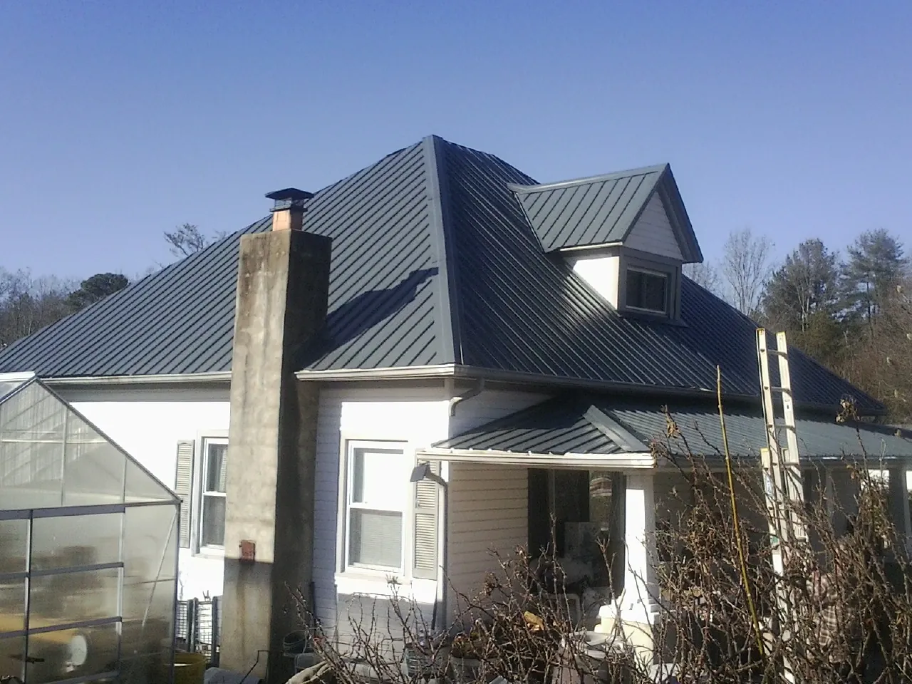 Dark blue standing seam metal roof on a white farmhouse with dormer — Slate & Tile Roof Repair by Roofing Brothers in Walnut Bottom