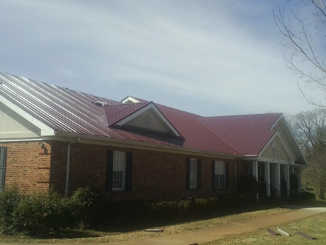 Red metal roof with gabled entries on a long brick building, from a Hail Damage Roof Repair job in Walnut Bottom