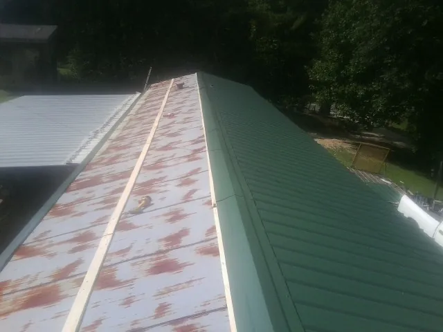 Old rusted panels beside newly installed green metal roofing — Wind Damage Roof Repair by Roofing Brothers in Walnut Bottom