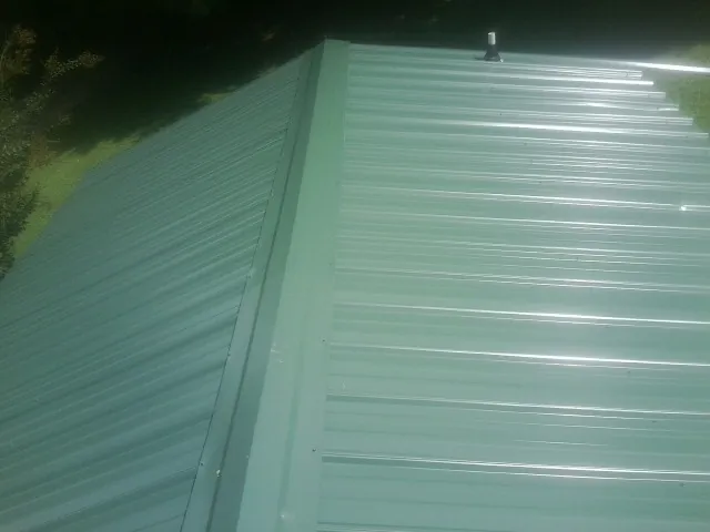 New green metal panels meeting at the ridge of a roof — Flat Roof Repair work by our crew in Walnut Bottom