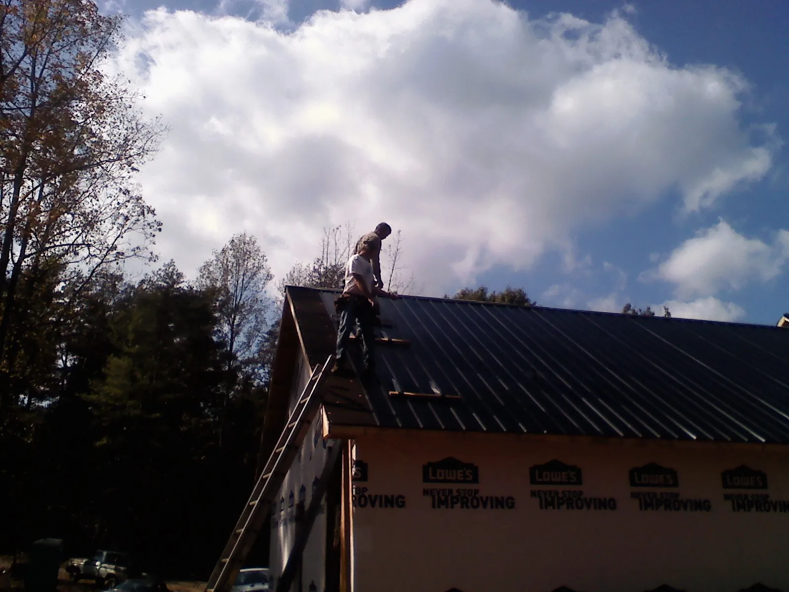 Roofer fastening dark metal panels high against a cloudy sky, from a Roof Inspection job in Walnut Bottom