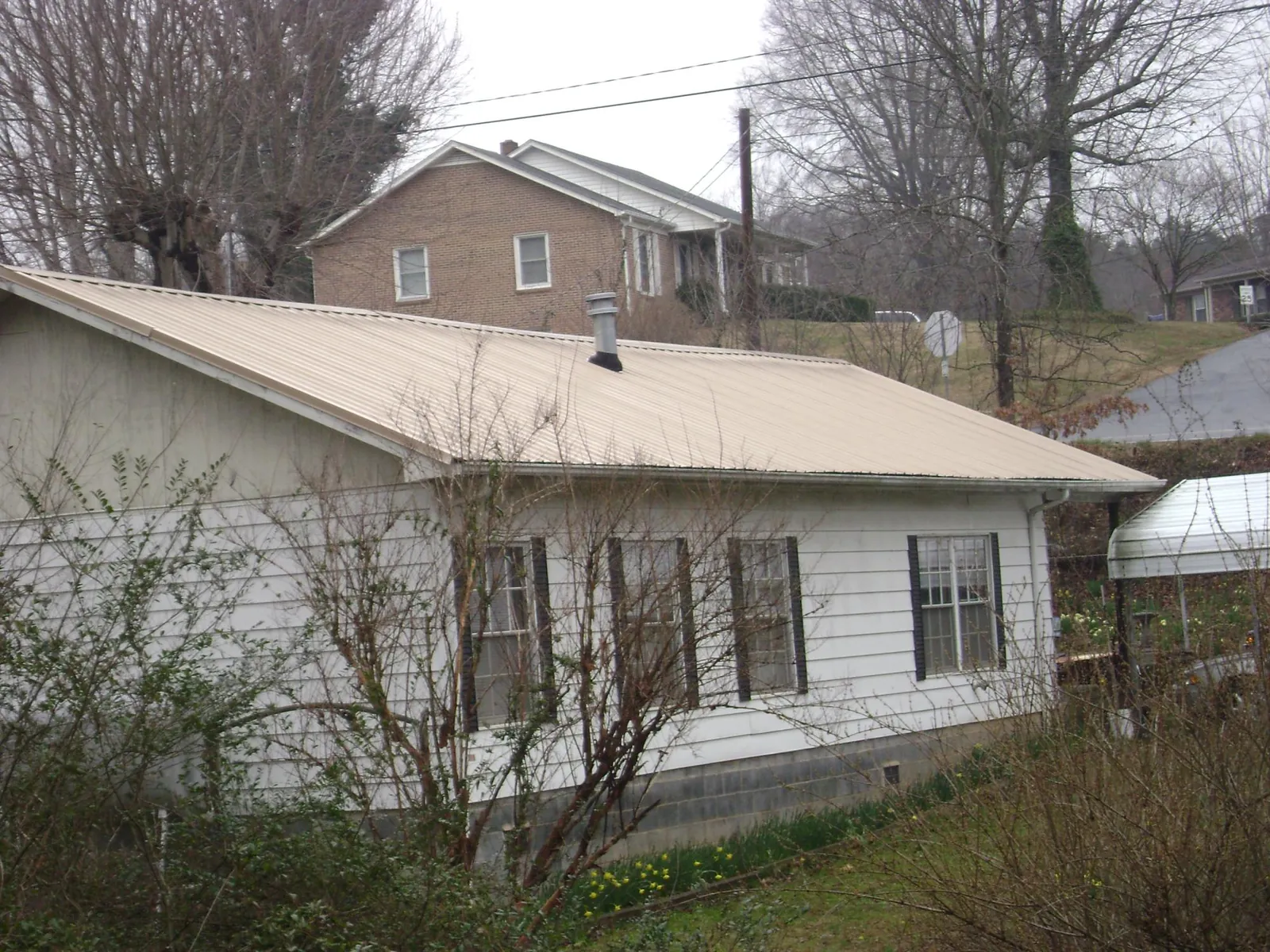 Tan metal roof on a white sided house set into a hillside — Commercial Roofing by Roofing Brothers in Walnut Bottom